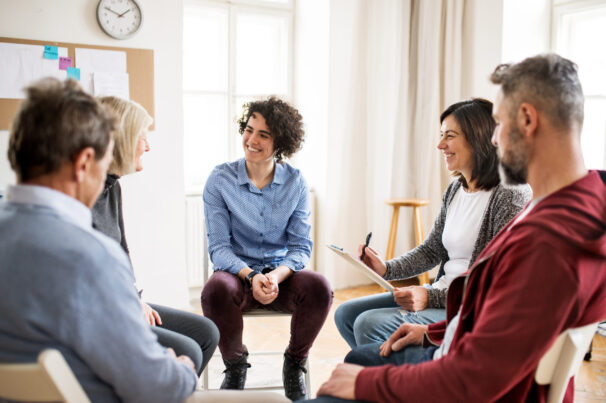 Serious men and women sitting in a circle during group therapy, talking.